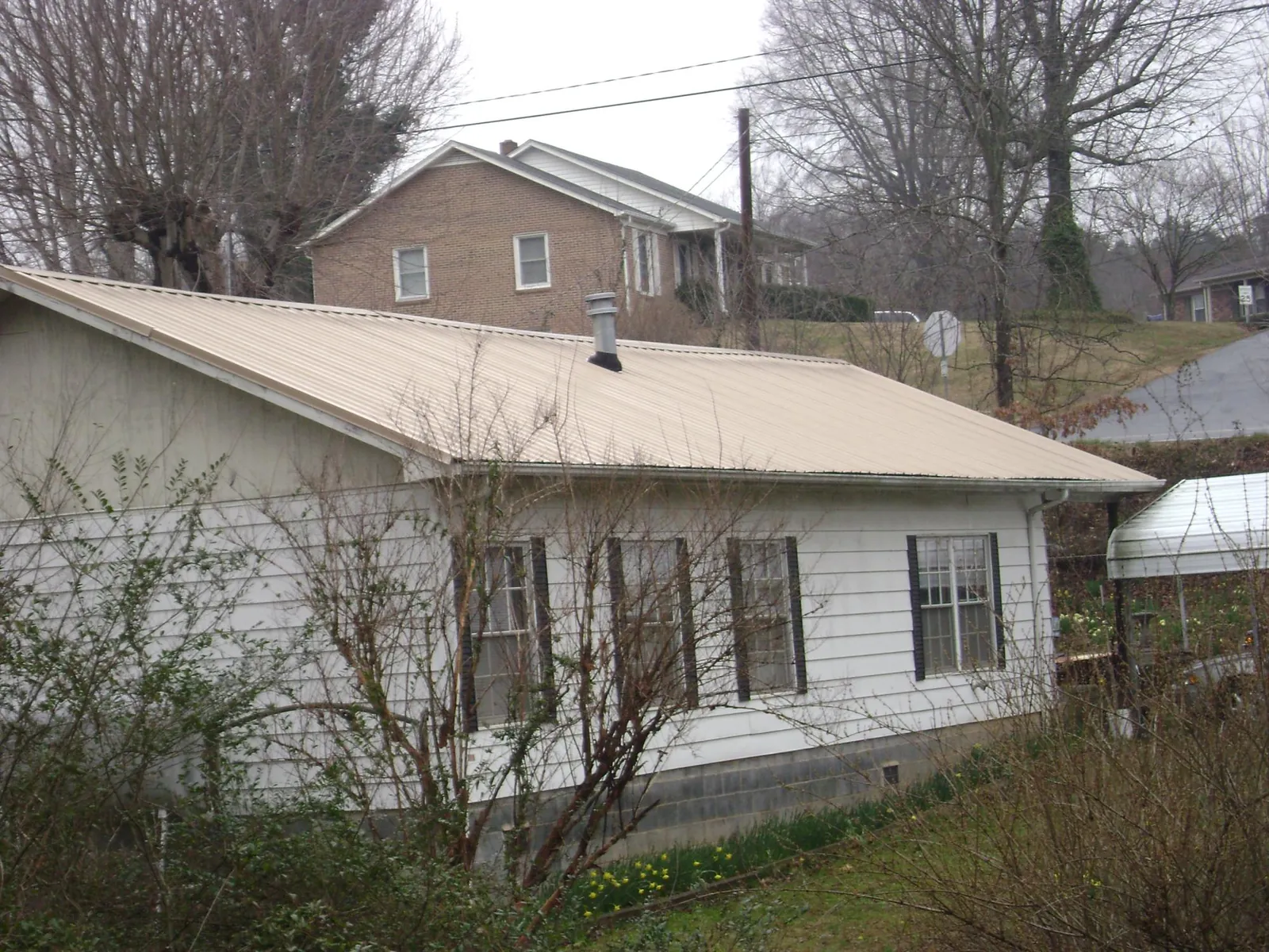 Tan metal roof on a white sided house set into a hillside — Commercial Roofing by Roofing Brothers in Kelso